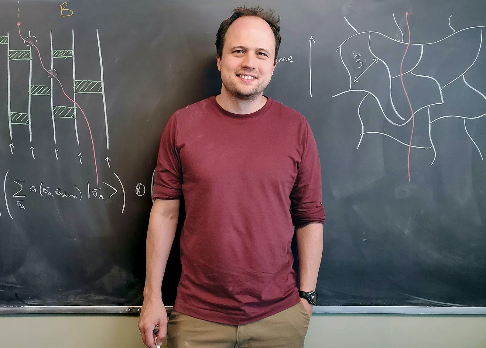 Brian Skinner standing in front of a blackboard, wearing a burgundy T-shirt. The board has a few diagrams drawn on it.