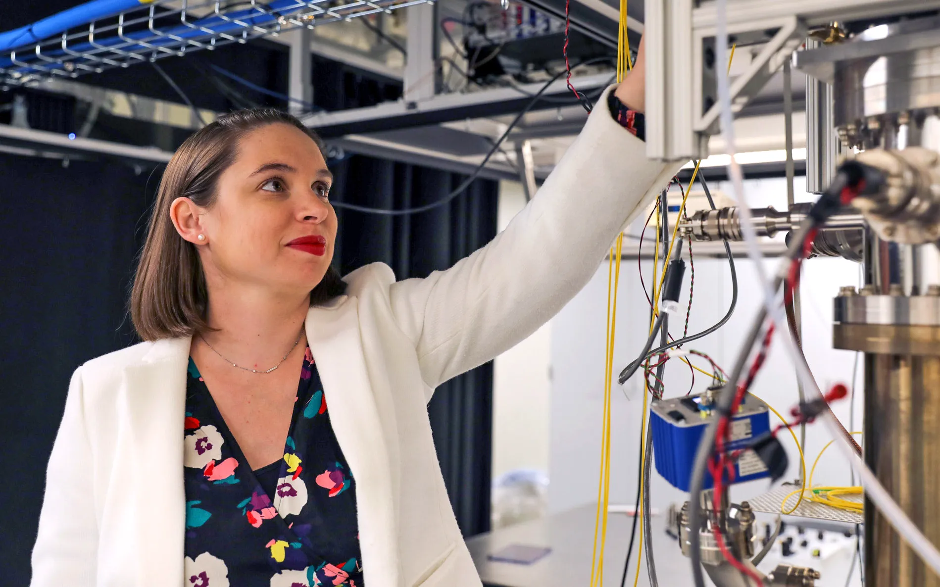 A portrait of Noel in a laboratory. She is smiling and wearing a white jacket and a flowered shirt.