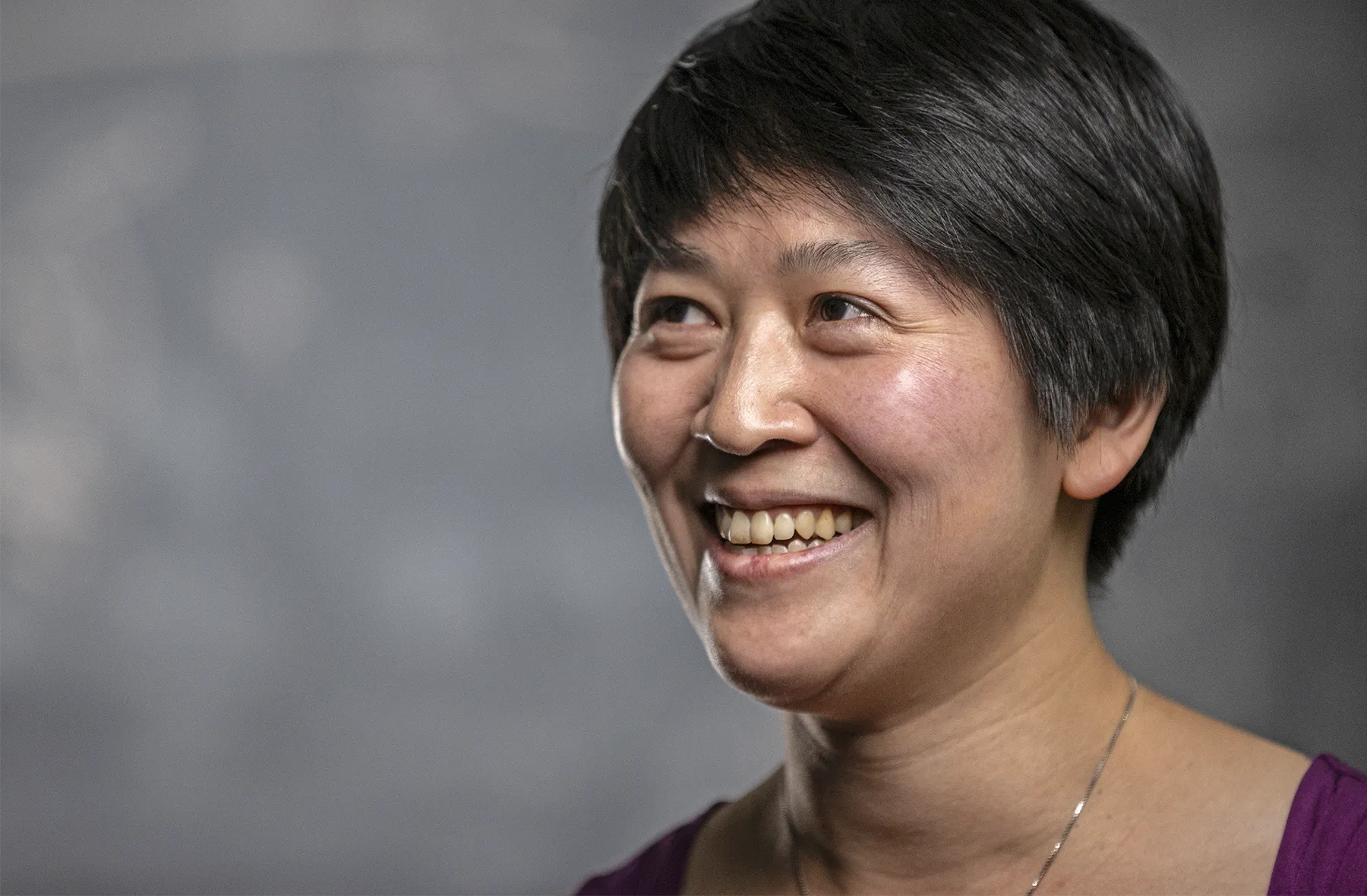 A headshot of Chiang smiling, with a blurry blackboard in the background.