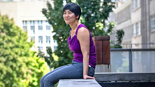 Cynthia Chiang on the McGill University campus. She is perched on a concrete wall, wearing a purple shirt and gray jeans, and the Montreal skyline is in the background.