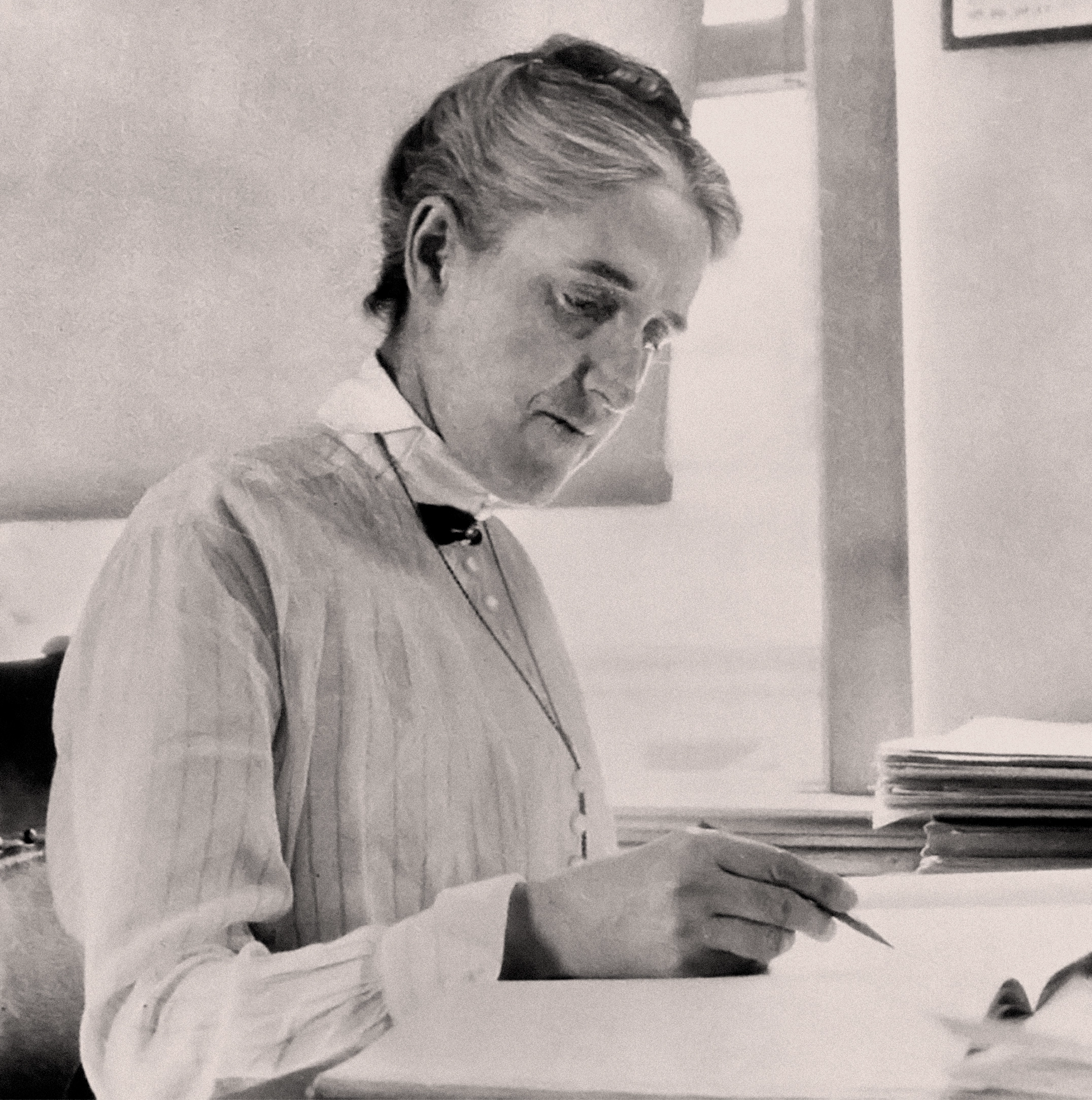 A black-and-white image of Henrietta Swan Leavitt. She is at her desk, writing in a notebook.