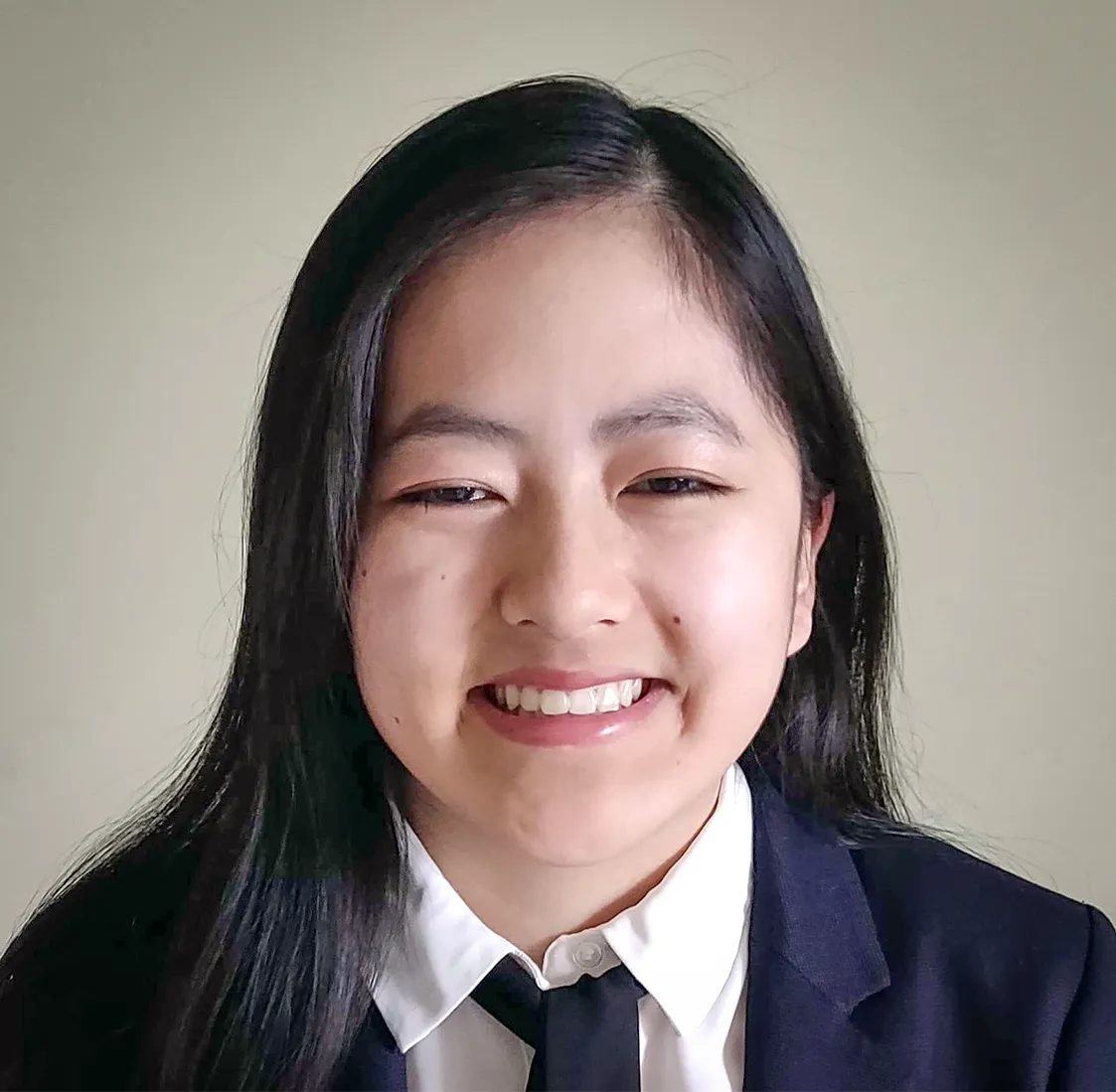 Laura Lewis in a coat and black tie, posing in front of a cream-colored background and smiling.