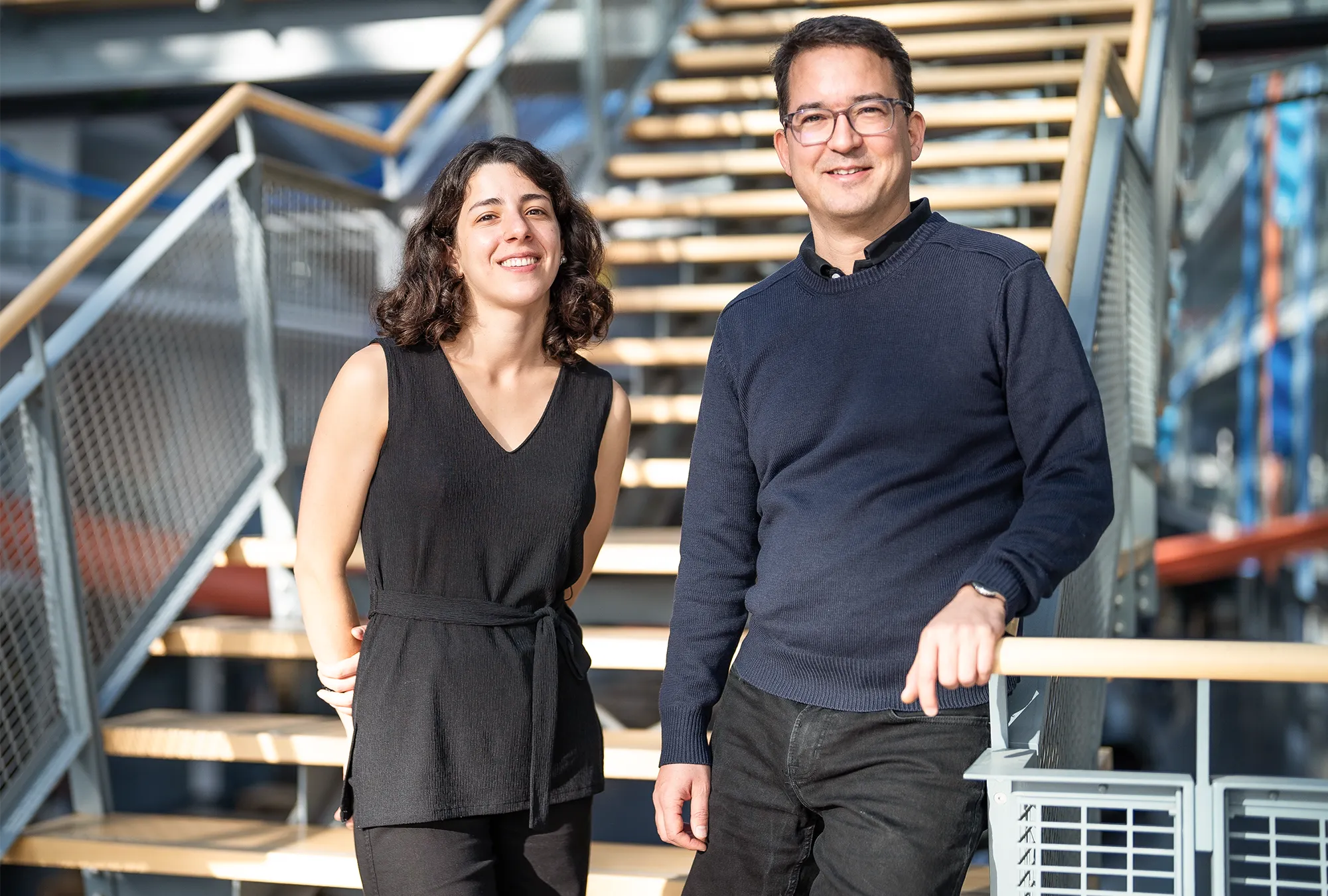 A man and woman stand together in front of a staircase.