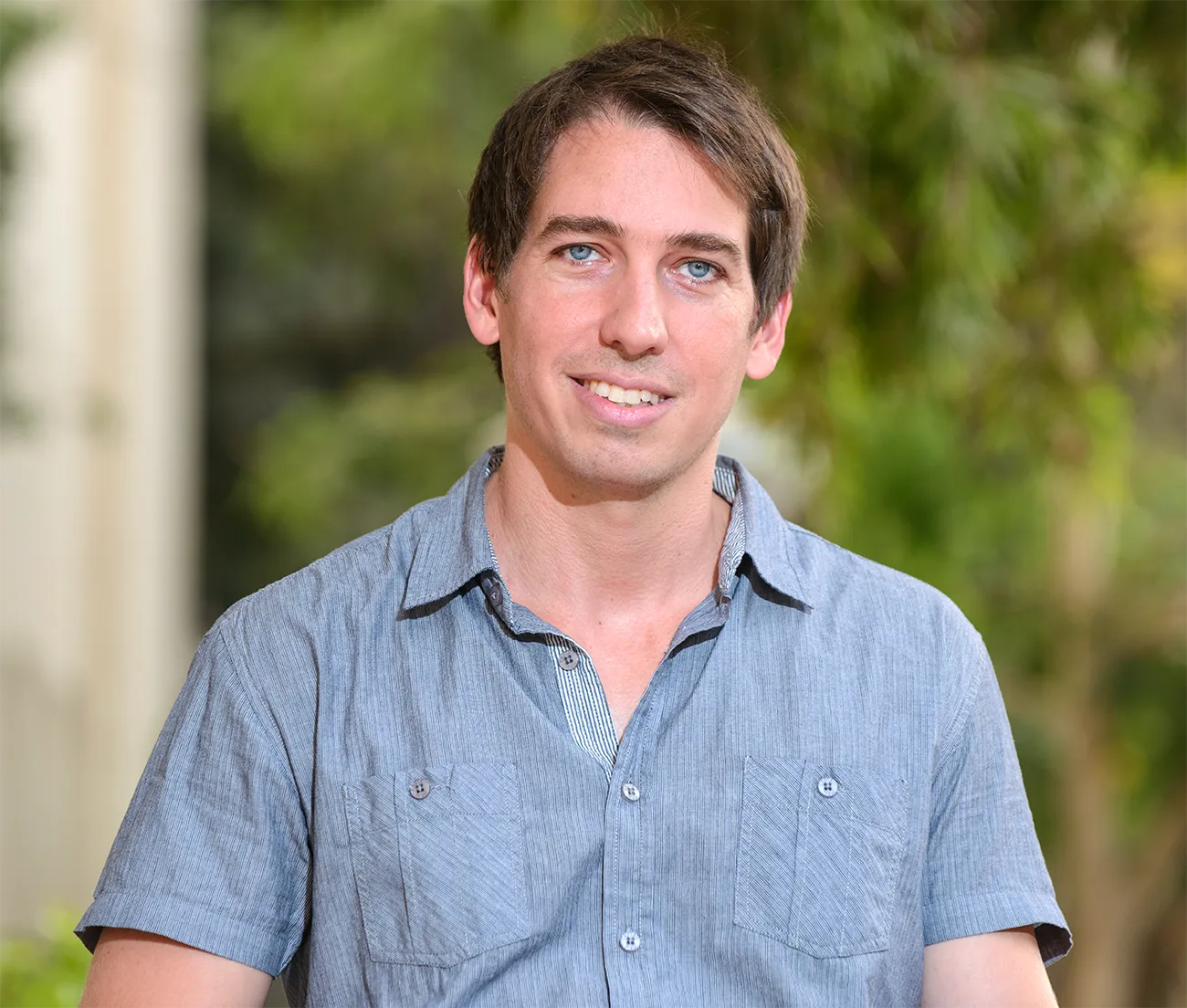 Ronen Eldan in a blue short-sleeved shirt against a blurry green background.