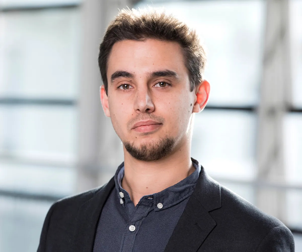 Antoine Cully in a black blazer and shirt standing in front of windows.