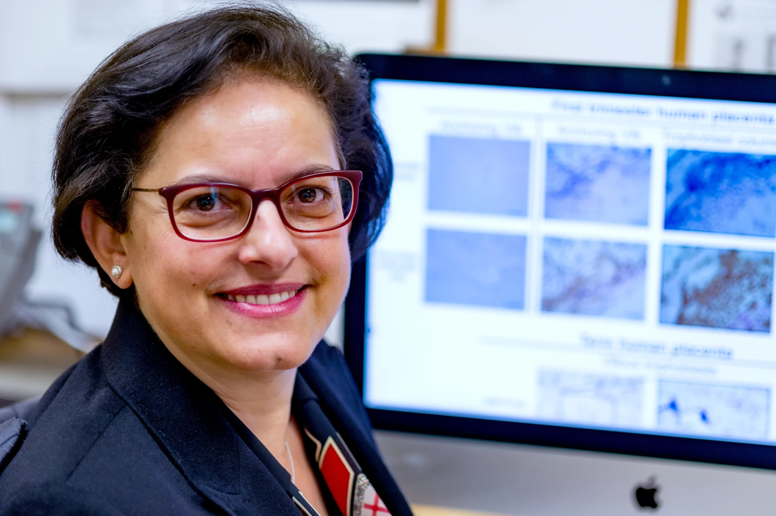 Hana Totary-Jain looks at the camera while sitting in front of a computer monitor.