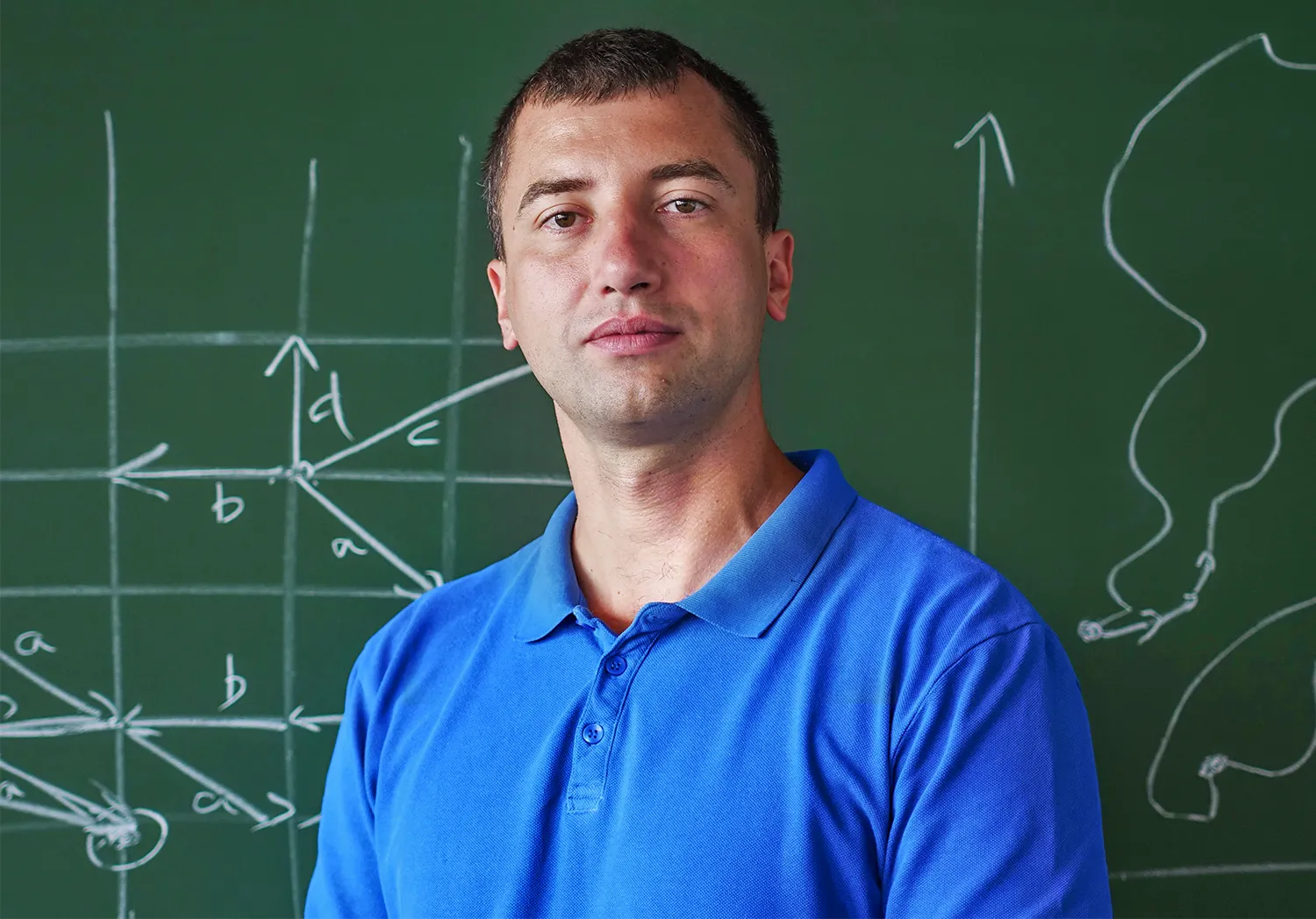 Wojciech Czerwiński in a blue polo shirt stands in front of a chalkboard.