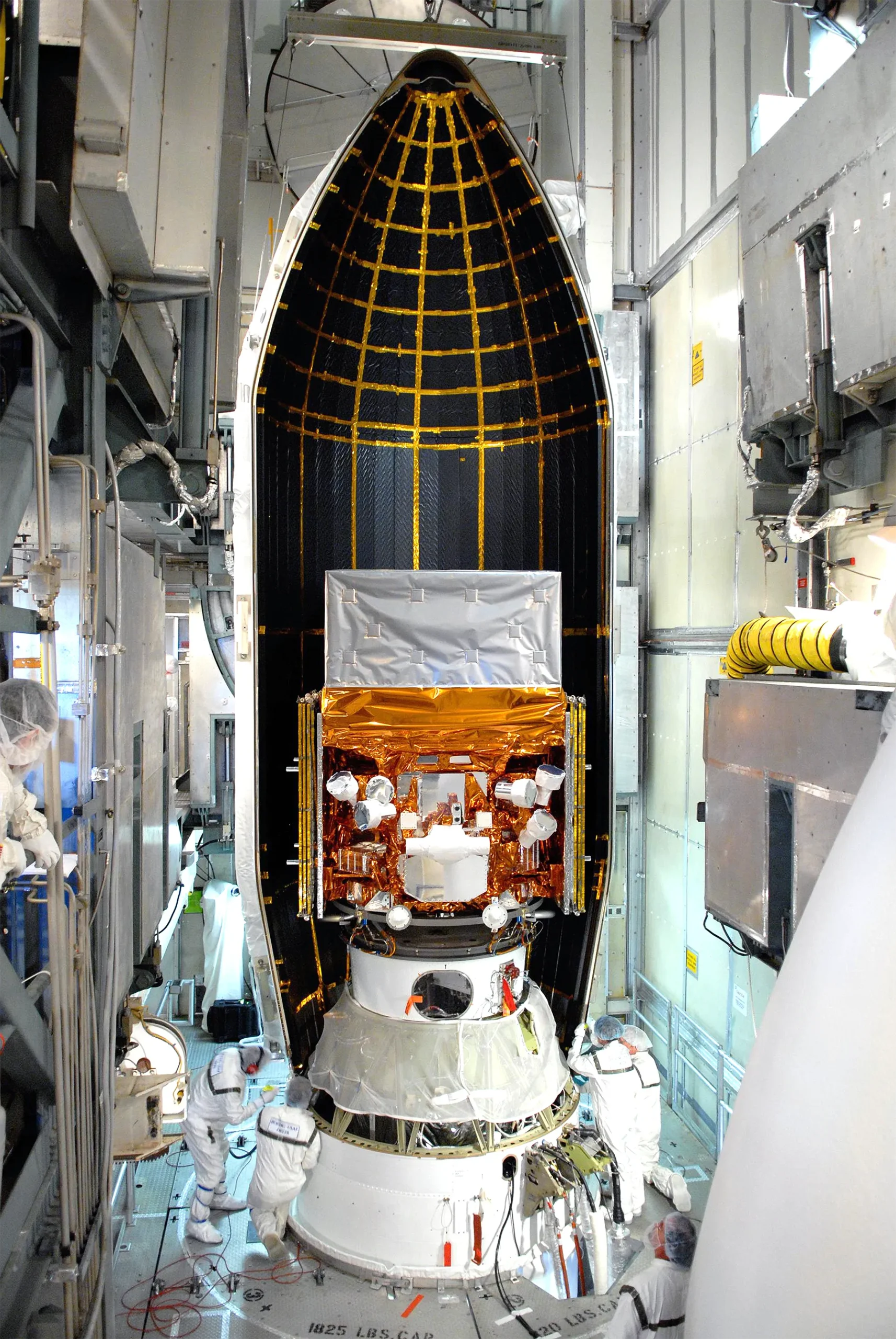 NASA’s Fermi Gamma-ray Space Telescope, about to be enclosed in a rocket faring. Four technicians in clean suits are working on the rocket.