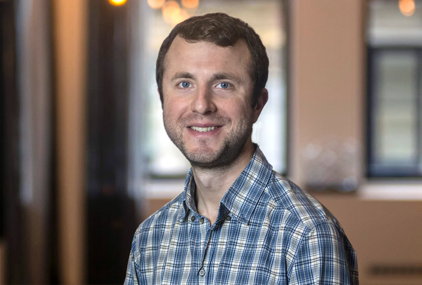 J. Colin Hill wearing a teal plaid shirt and smiling.