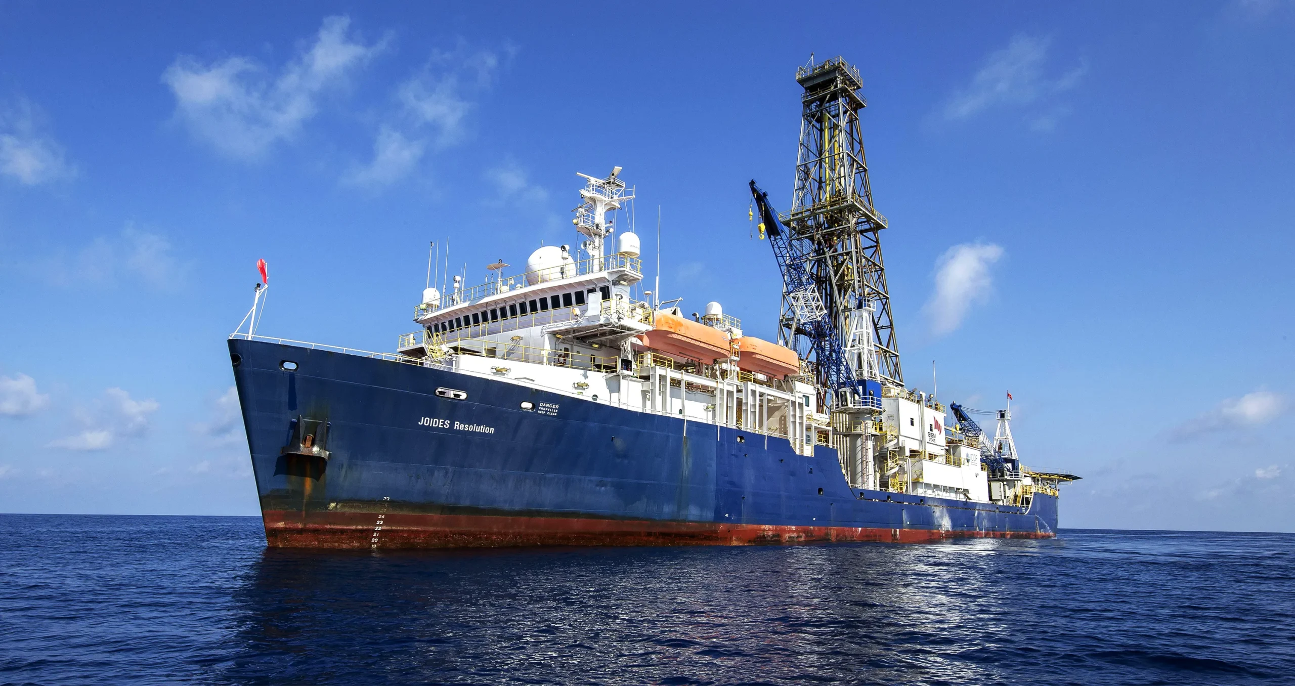 The ship JOIDES Resolution, which can drill deep beneath the ocean floor. Its hull is blue, and the decks are full of equipment.