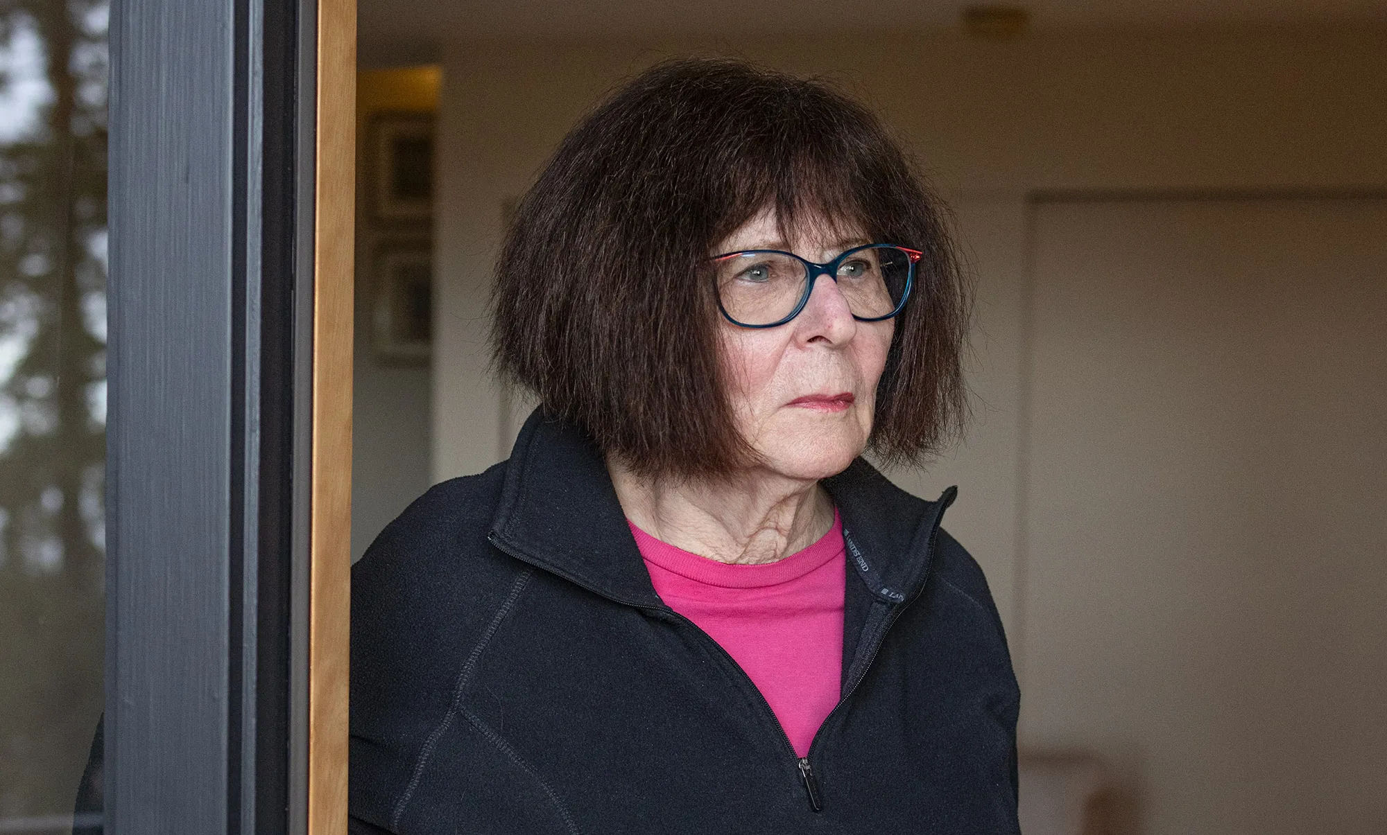 Lenore Blum in a black sweater stands by a window looking into the distance