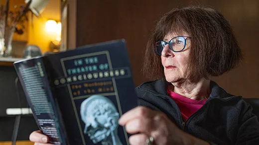 Lenore Blum, in a black sweater, reads In the Theater of Consciousness