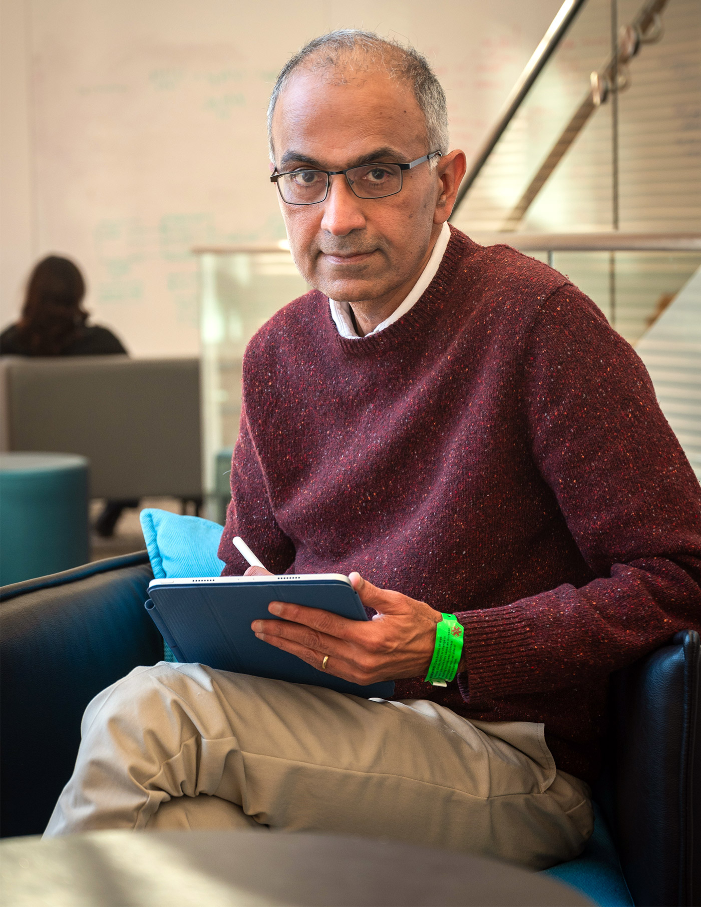 Sanjeev Arora in a red sweater sits and writes on a tablet