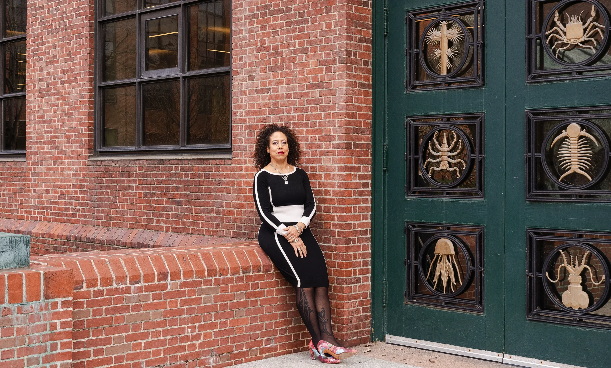 Extavour leans against the wall near the ornate doors of the Biological Laboratory building at Harvard University, which are decorated with bronze sculptures of jellyfish, scorpions and other invertebrates.