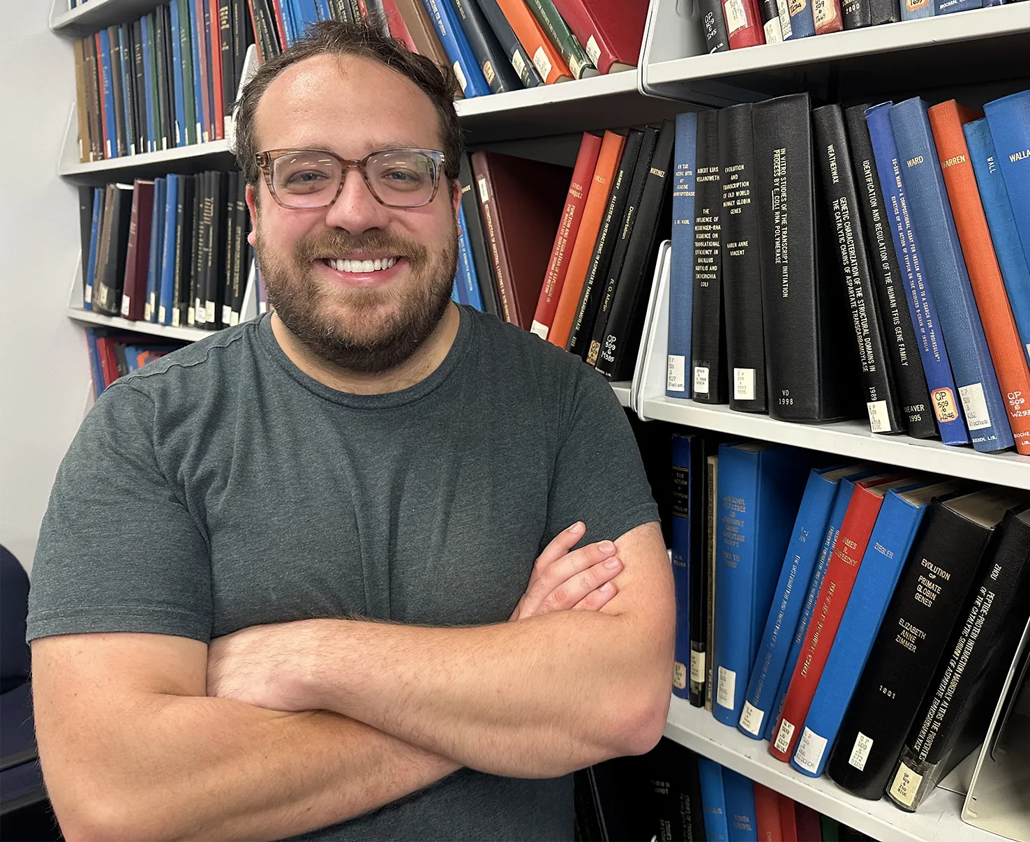 Photo of researcher Connor Horton, standing with folded arms beside a bookcase.