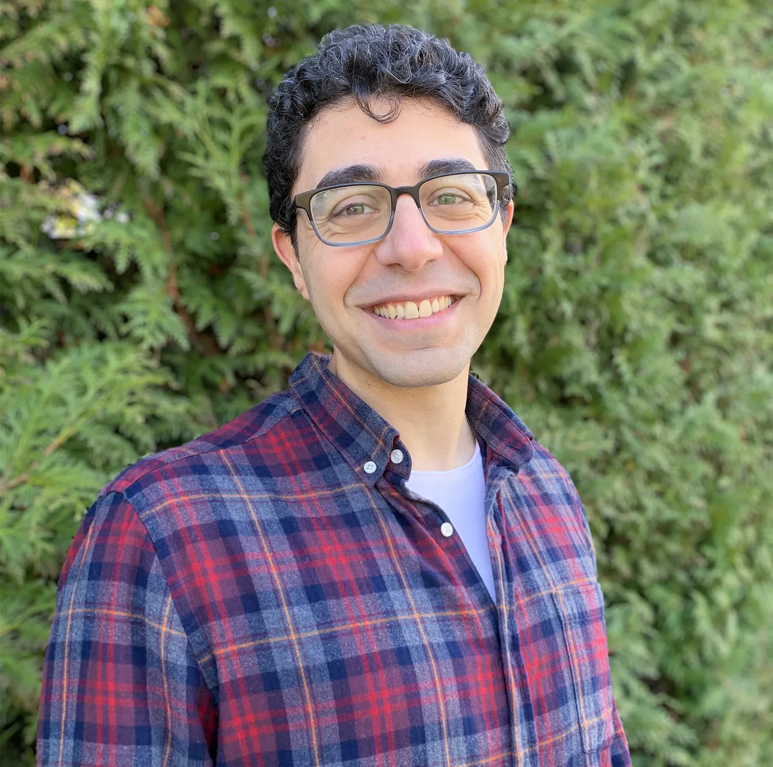 A portrait of Georges Obied. He’s wearing a plaid shirt and smiling.