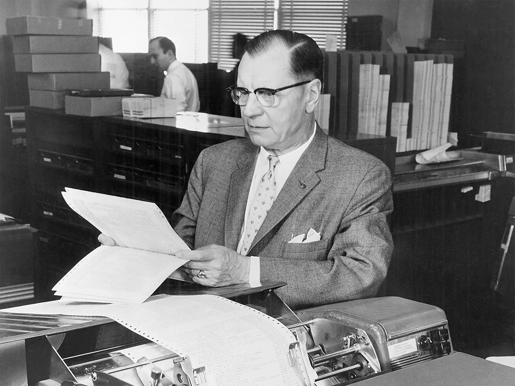 Black and white photo of Hans Peter Luhn in a suit, reading a piece of paper.