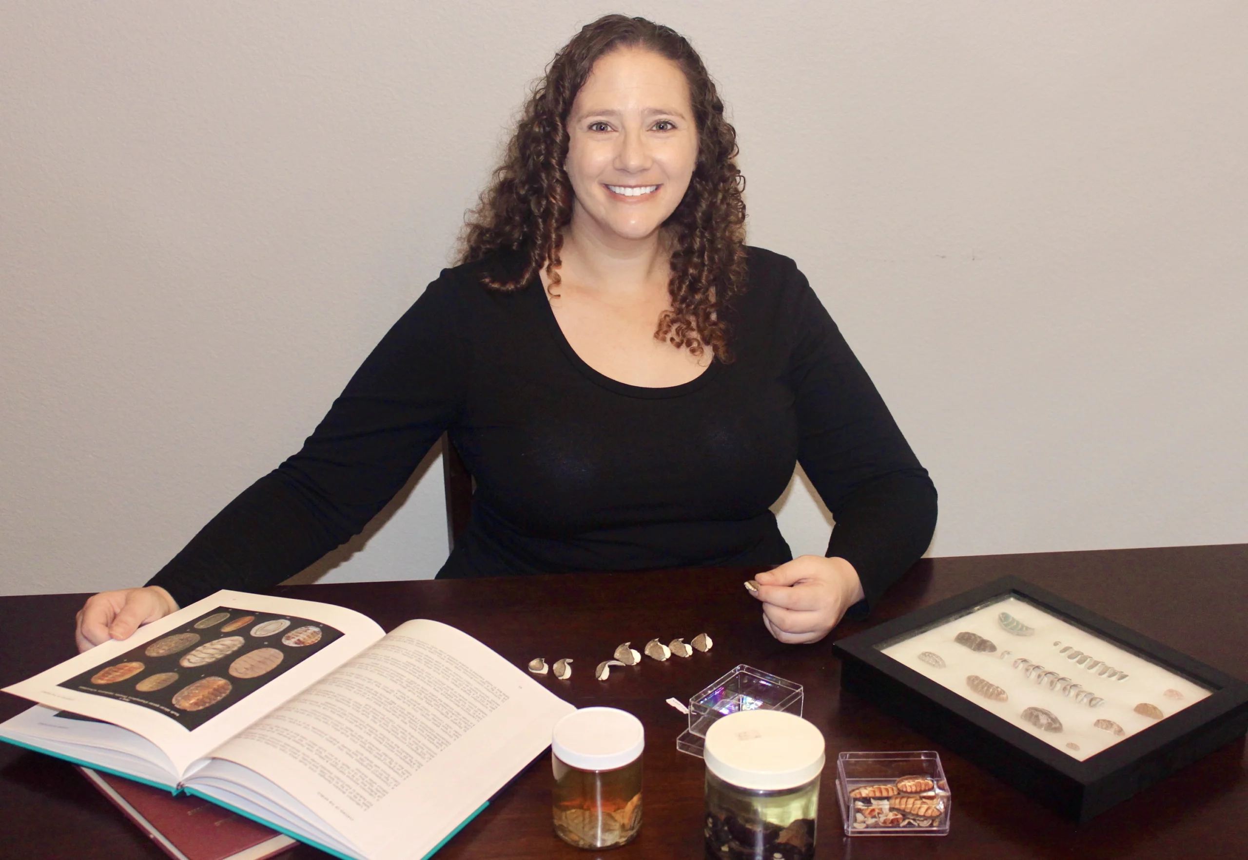 Rebecca Varney examines chitons specimens while sitting at a desk.