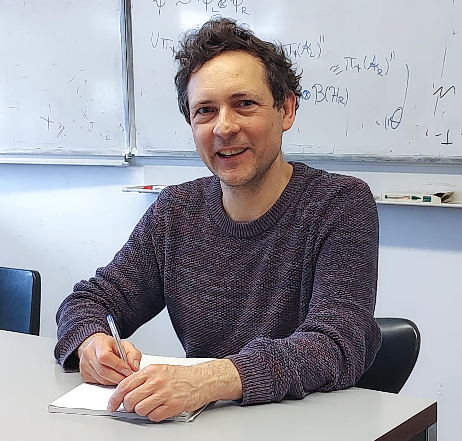 A man smiles while scribbling in a notebook.