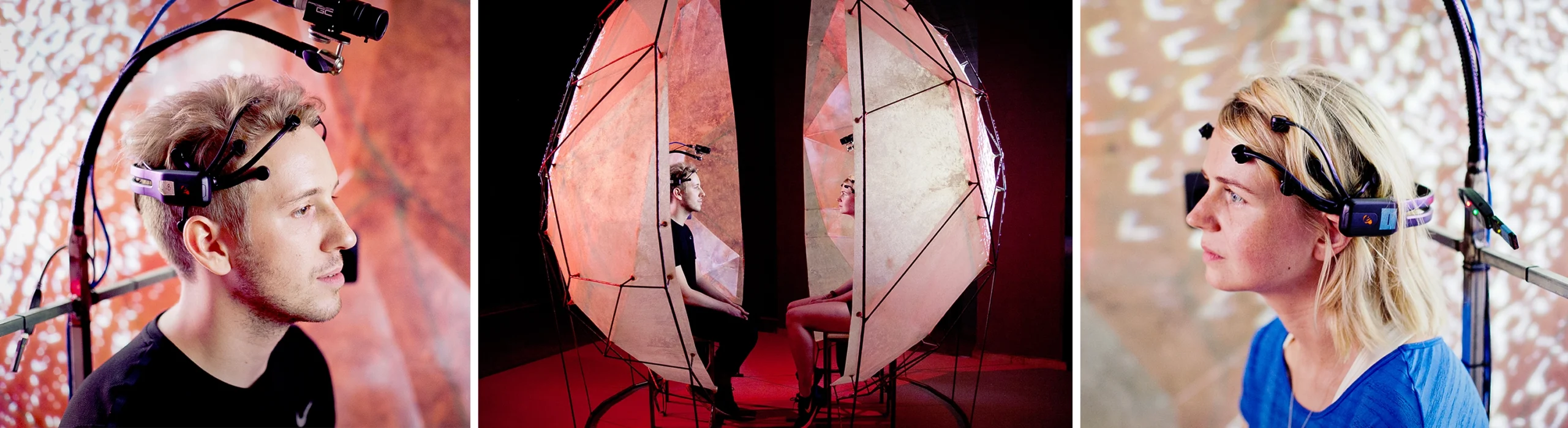 Two people sit facing each other, each inside a half-shell. They wear cameras and a neural device to measure their interbrain connection.