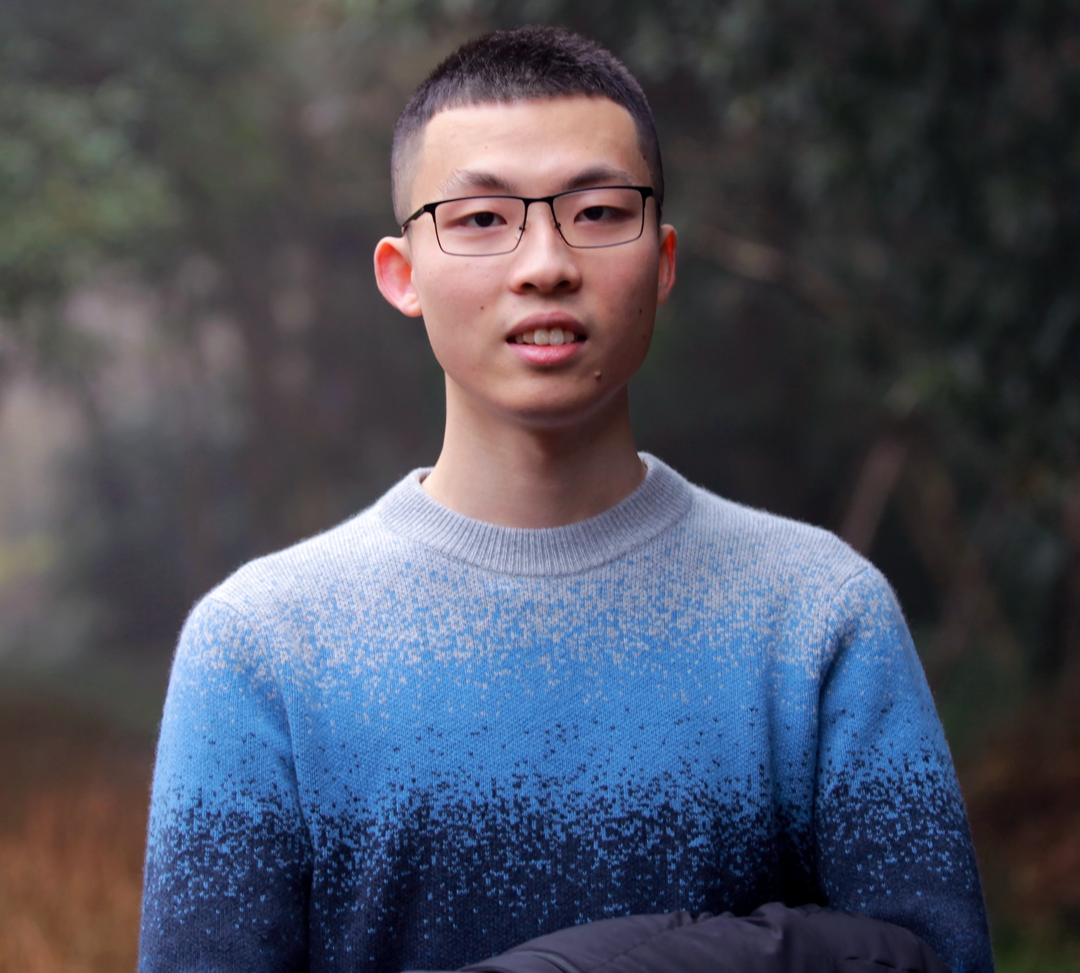 Renfei Zhou in a multicolored sweater in front of trees.