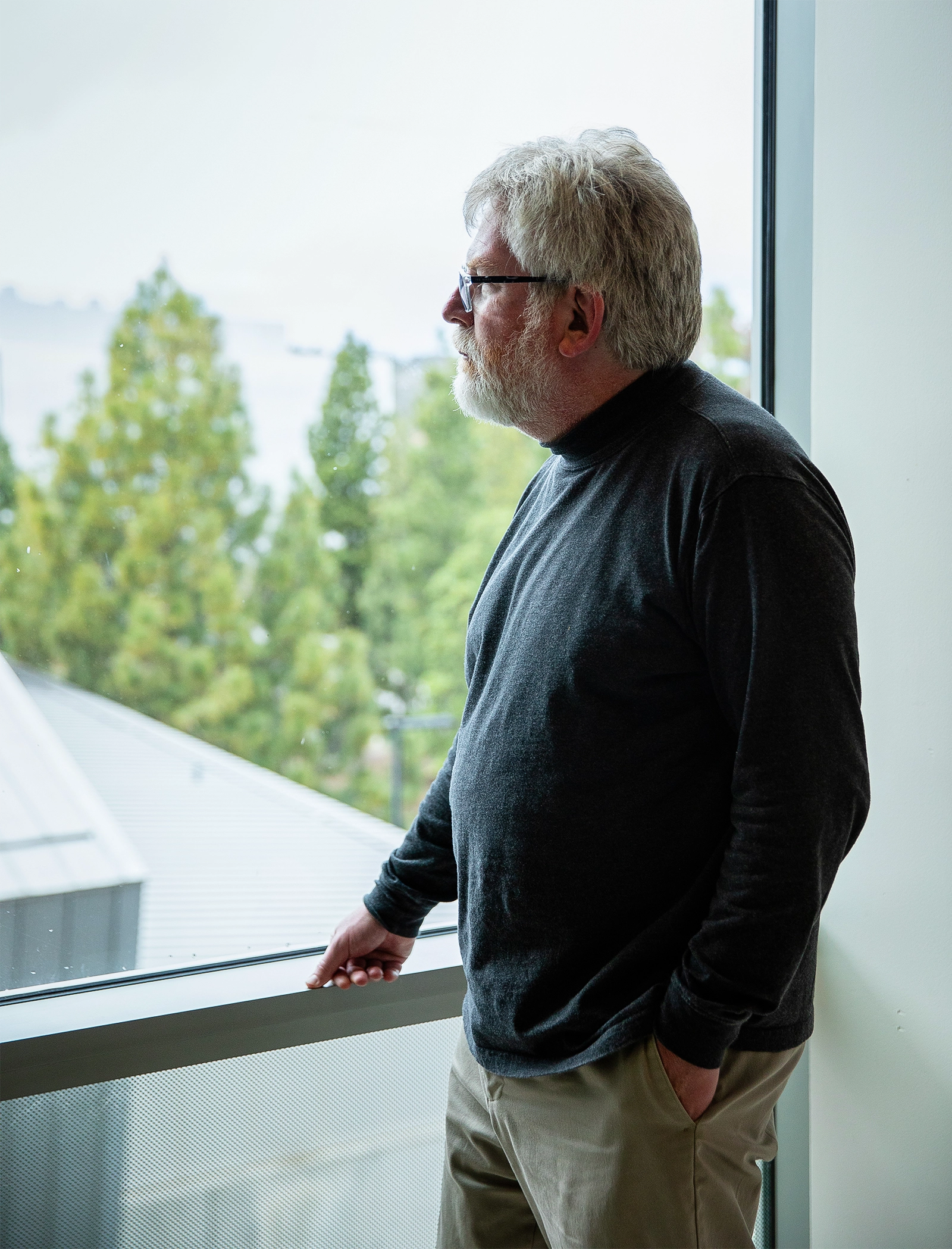 Russell Impagliazzo, in khakis and a dark shirt, looks out a window