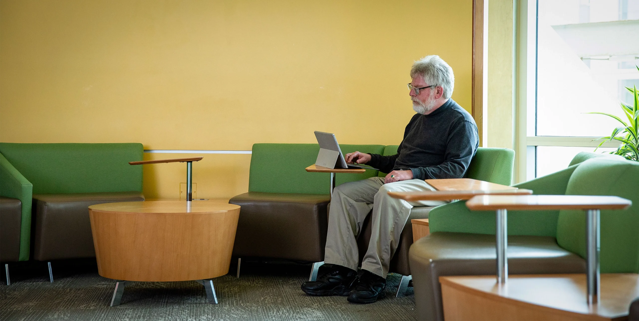 Russell Impagliazzo, in khakis and a dark shirt, sits in a yellow room and types on a tablet