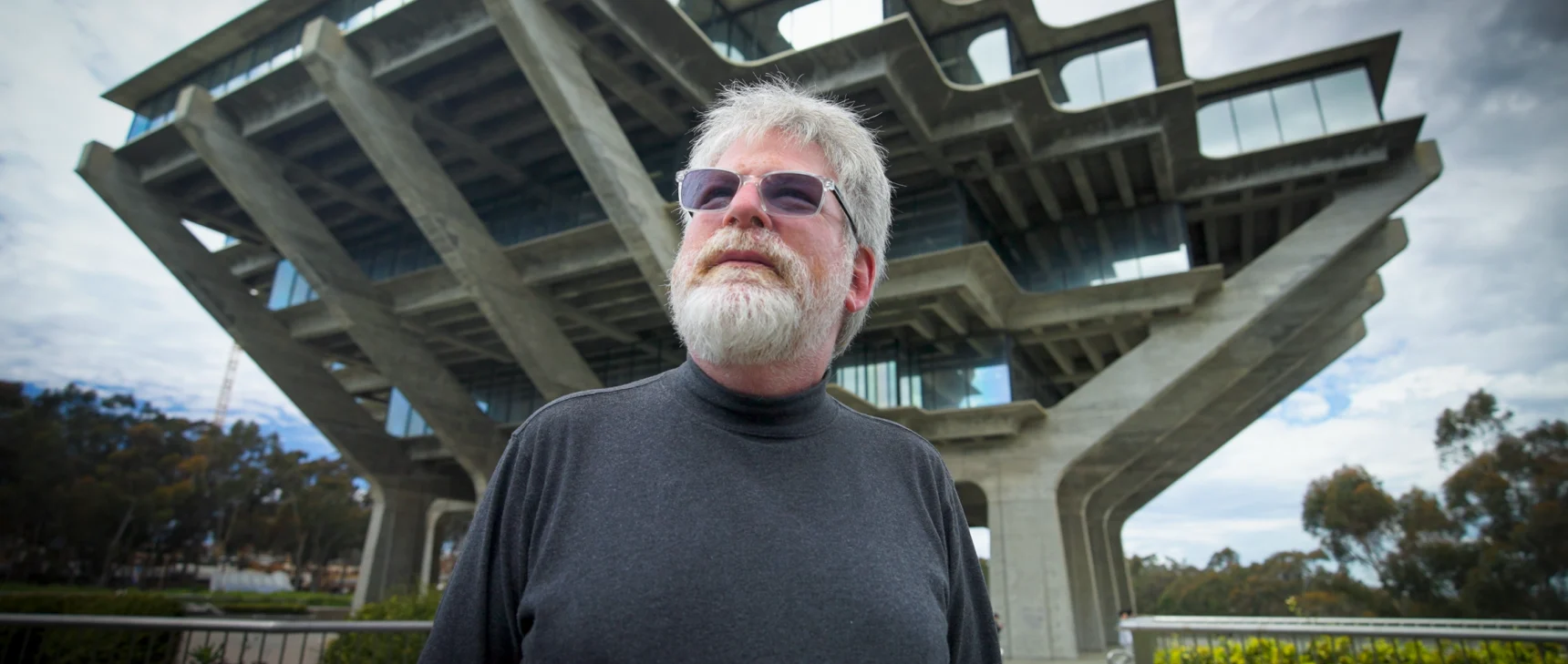 Russel Impagliazzo wearing a dark shirt and sunglasses stands outside a tree-shaped building