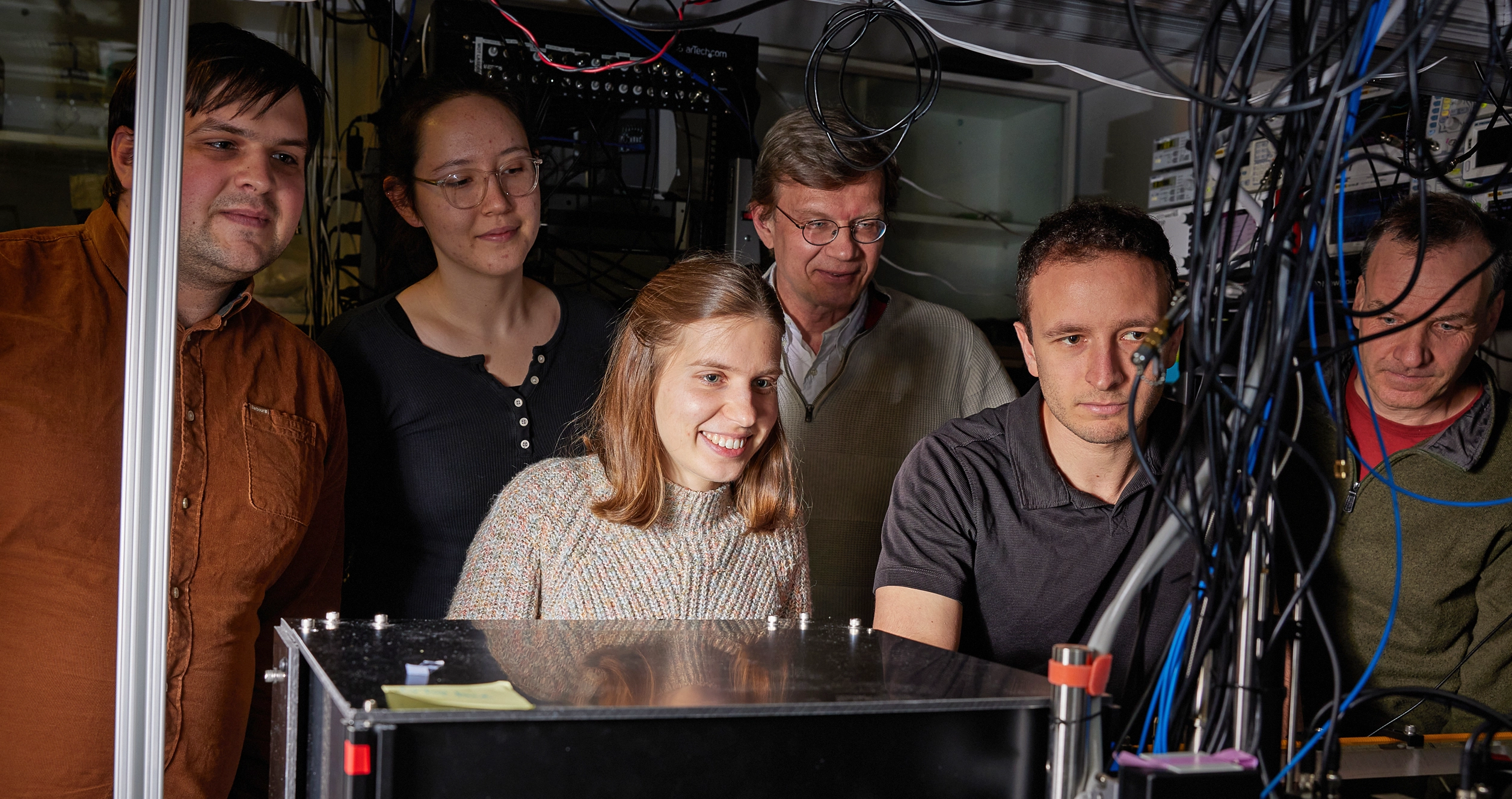 Six people with happy expressions crowd around an optical table.