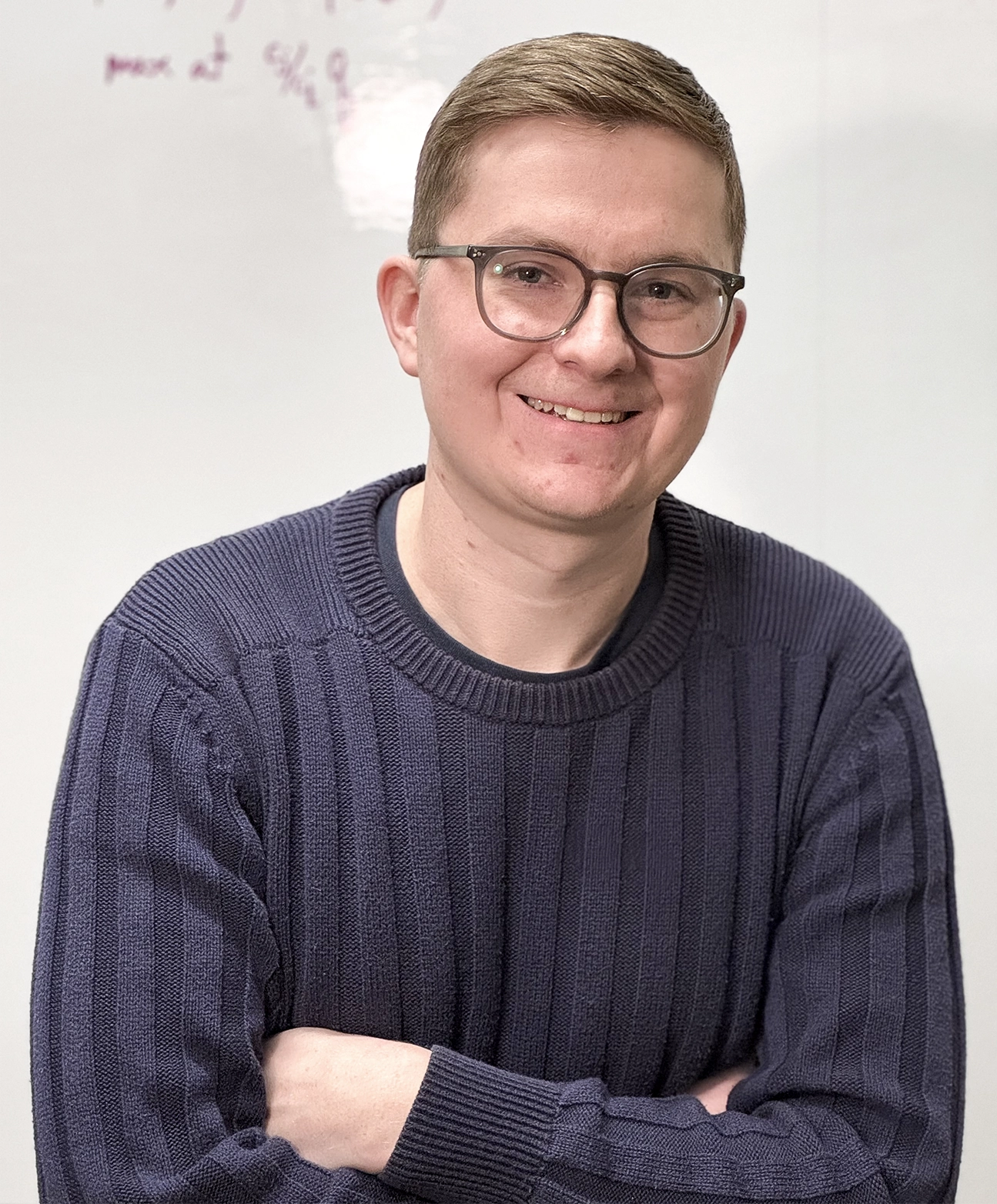 William Merrill in a blue sweater in front of a white board with an equation.