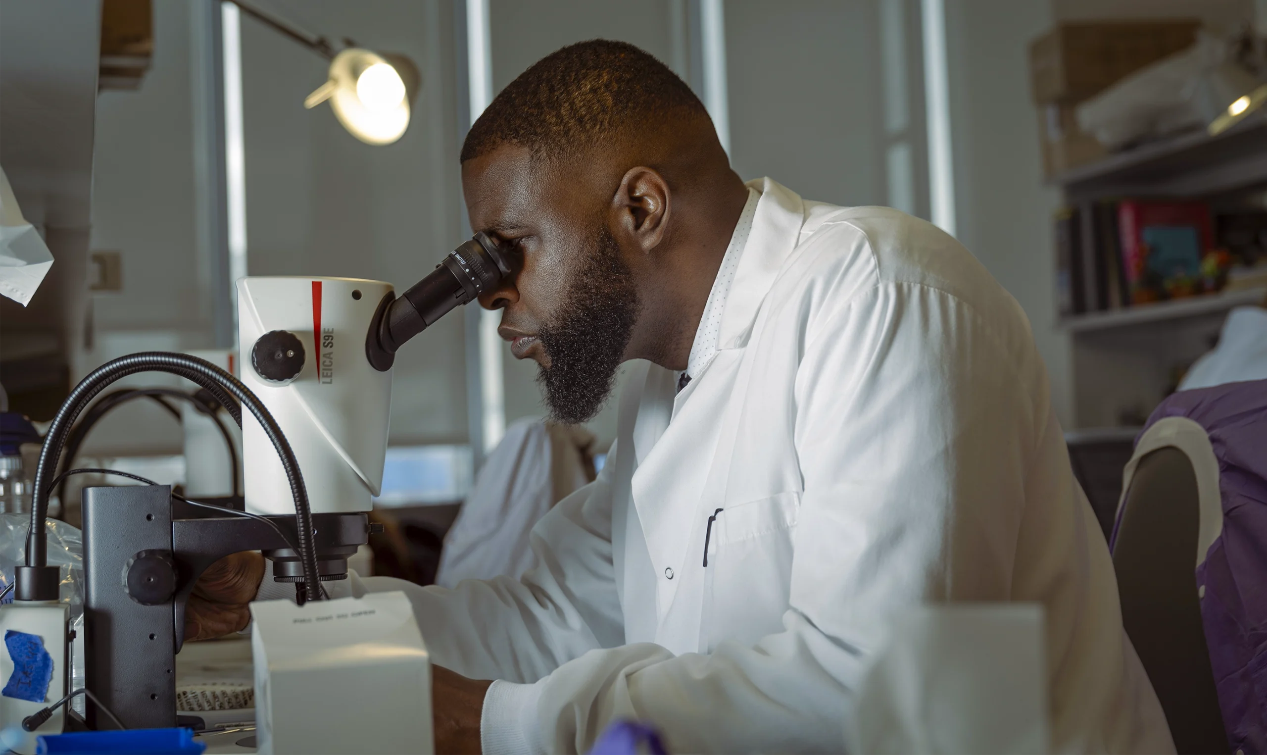 Neuroscientist Ishmail Abdus-Saboor, wearing a white lab coat, looks through a microscope in his lab at the Mortimer B. Zuckerman Mind Brain Behavior Institute of Columbia University.