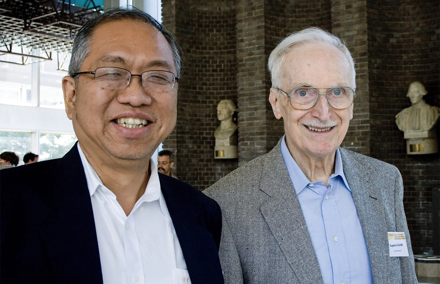 Two men wearing blazers stand together in an auditorium.