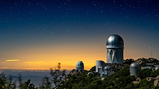 Photo of a telescope sitting atop a mountain beneath a starry sky.