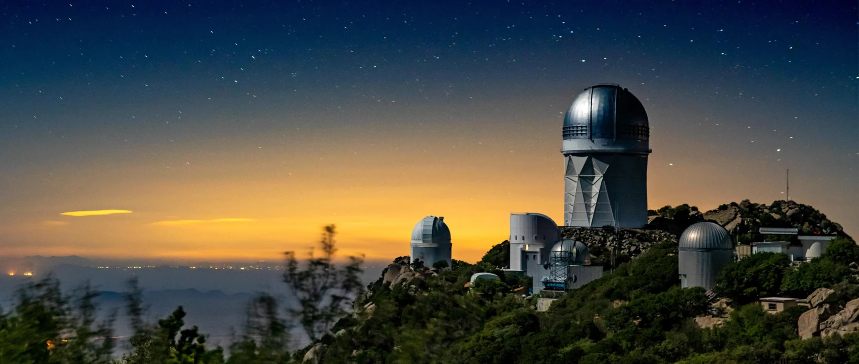 Photo of a telescope sitting atop a mountain beneath a starry sky.