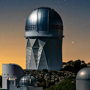 Photo of a telescope sitting atop a mountain beneath a starry sky.