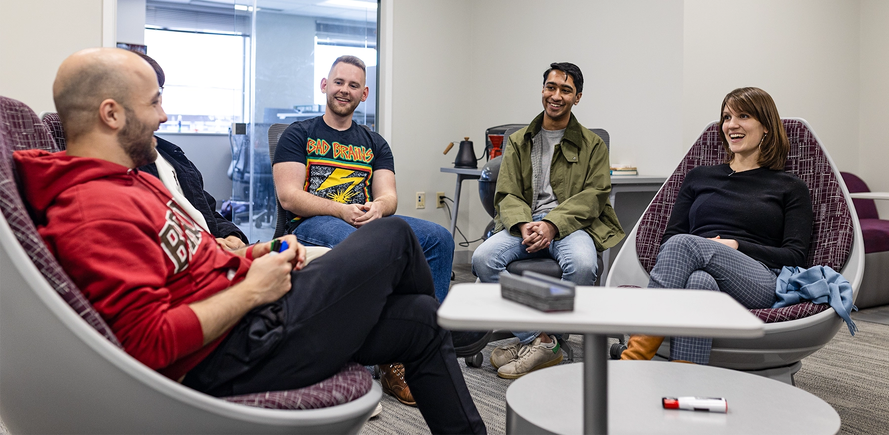 Ellie Pavlick and four students sit and talk within a lounge with white walls