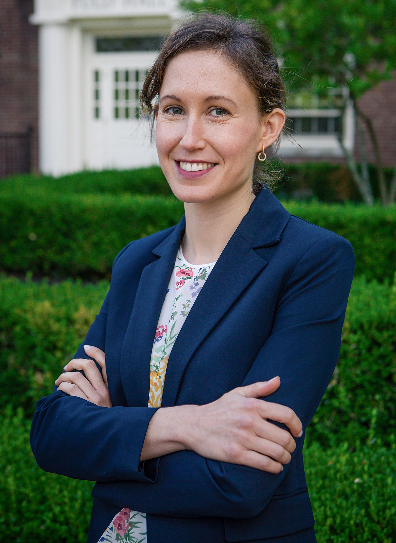 A woman standing outside in a blue blazer with her arms crossed smiles at the camera.