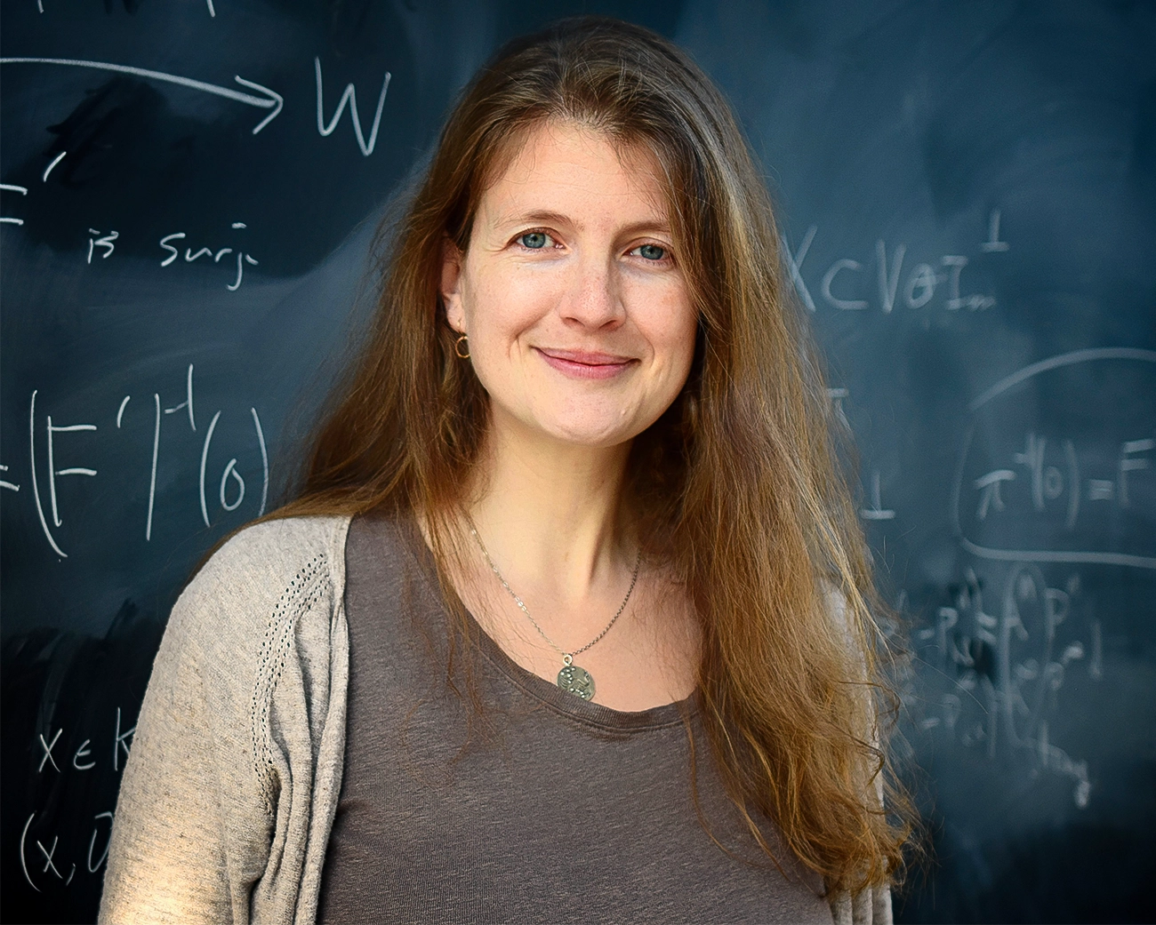 A smiling woman stands in front of a blackboard.