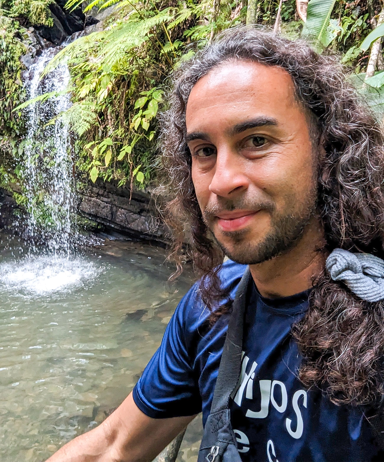 Sam Díaz-Muñoz stands in front of a waterfall.