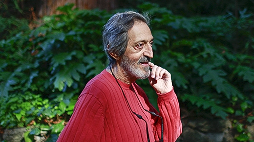 Avi Wigderson in a red sweater stands in front of rocks and a tree.