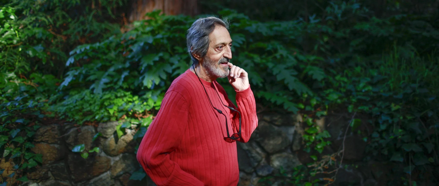 Avi Wigderson in a red sweater stands in front of rocks and a tree.