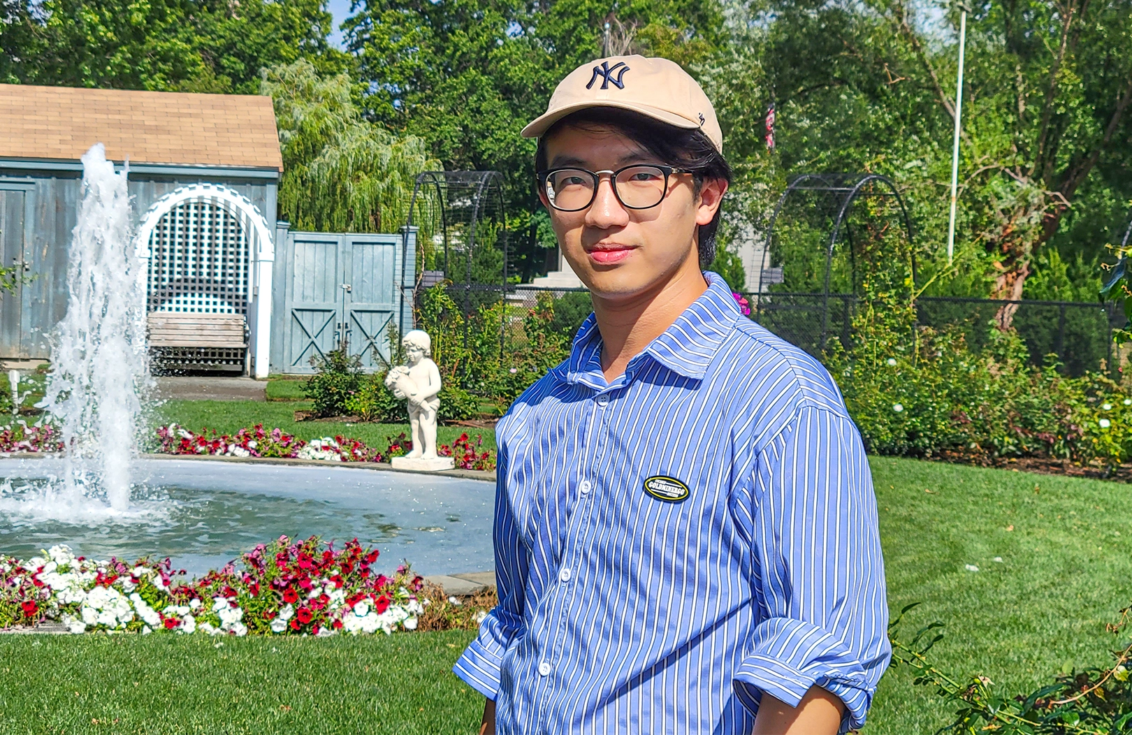 Ziming Liu in a striped blue shirt and Yankees baseball cap in front of a fountain.