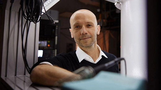 Close-up portrait of a man leaning against some equipment in a lab and smiling at the camera.