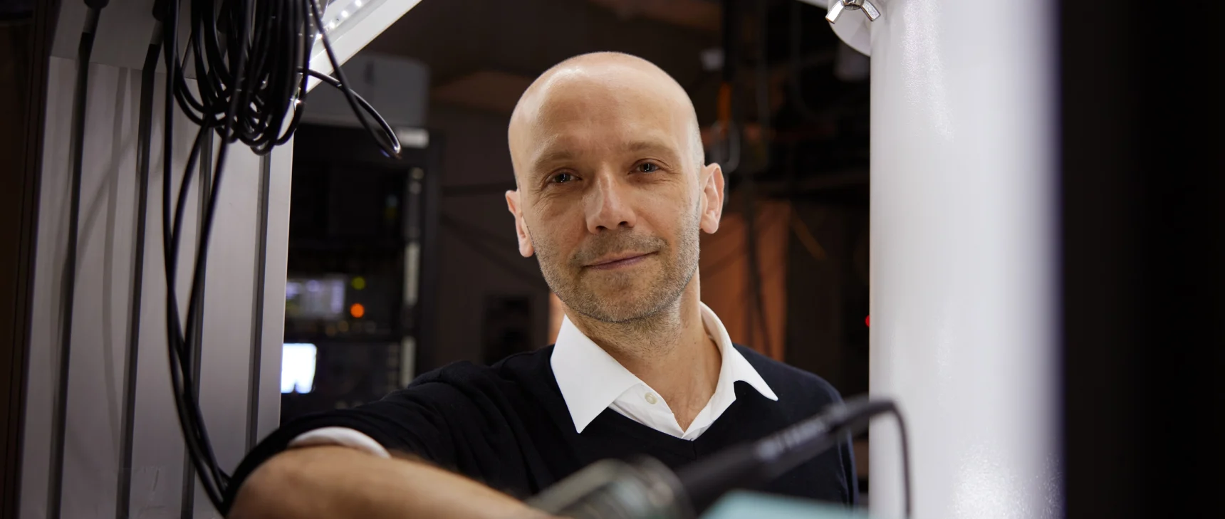 Close-up portrait of a man leaning against some equipment in a lab and smiling at the camera.