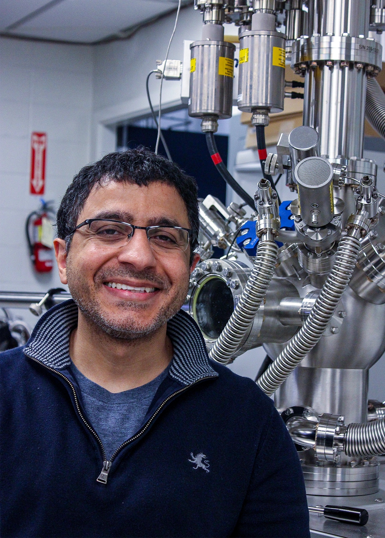 Bhavin Shastri in a blue shirt and sweater stands in his lab.