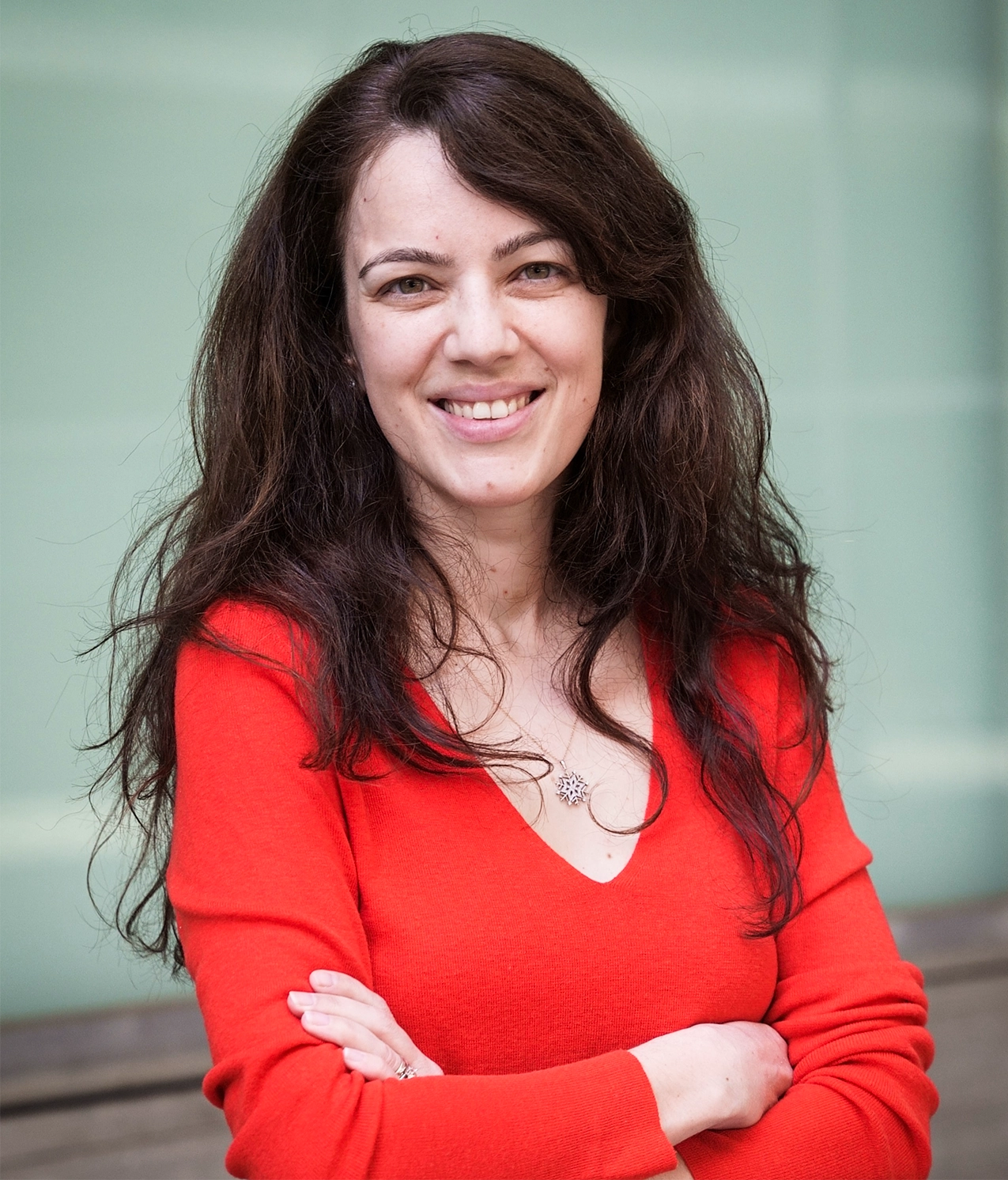 Elvan Böke portrait wearing a red shirt and smiling at the camera.