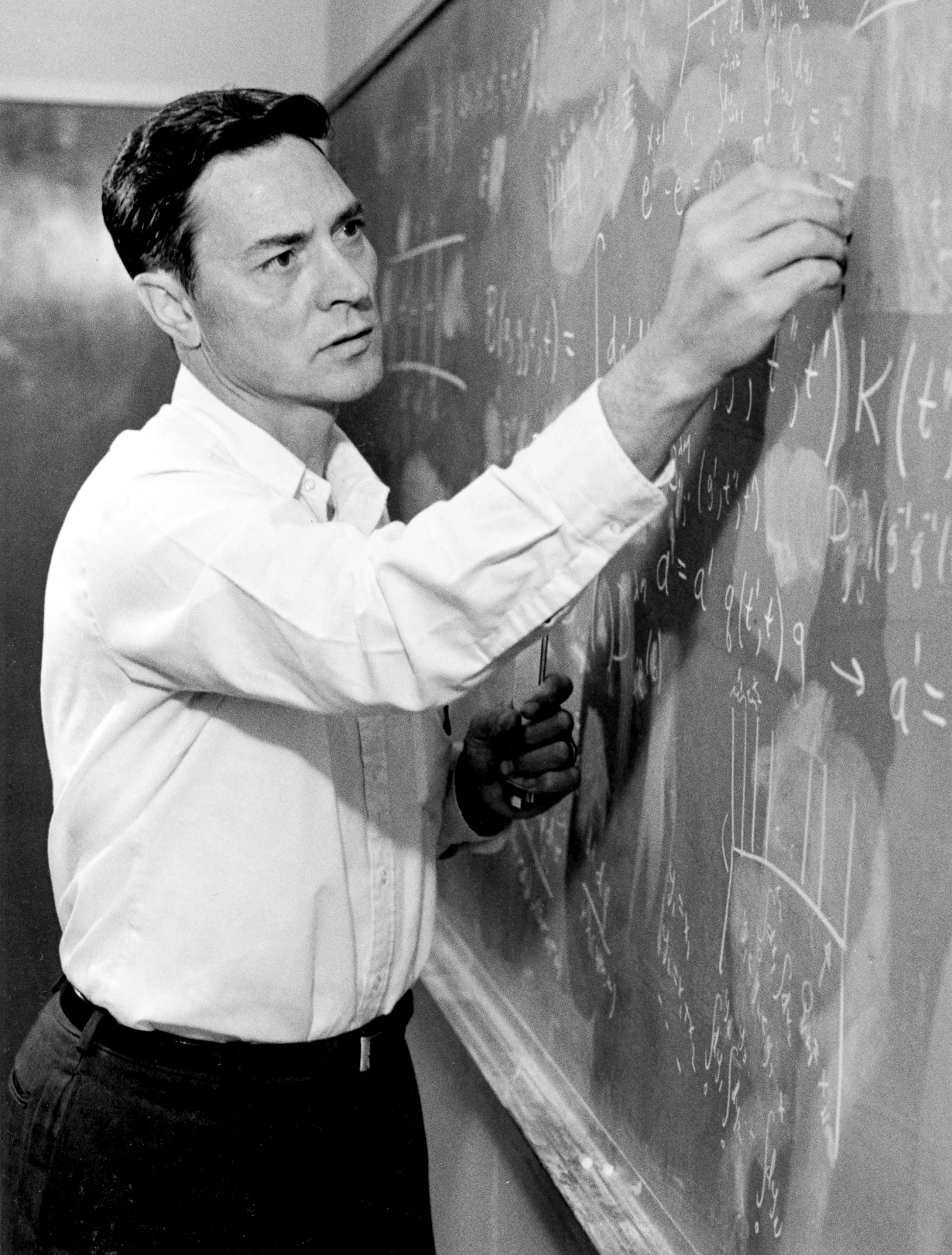 A man in a white shirt scrawls equations on a chalkboard.