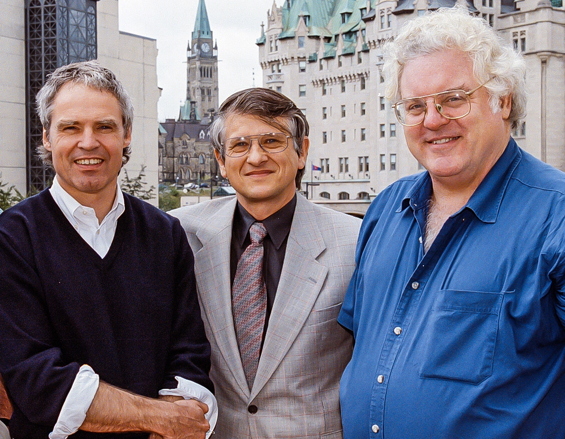 Three men stand together in front of a cityscape.