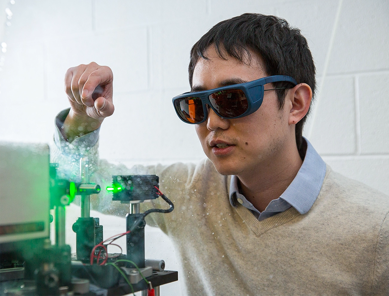 A man wears protective glasses and fiddles with a green laser.