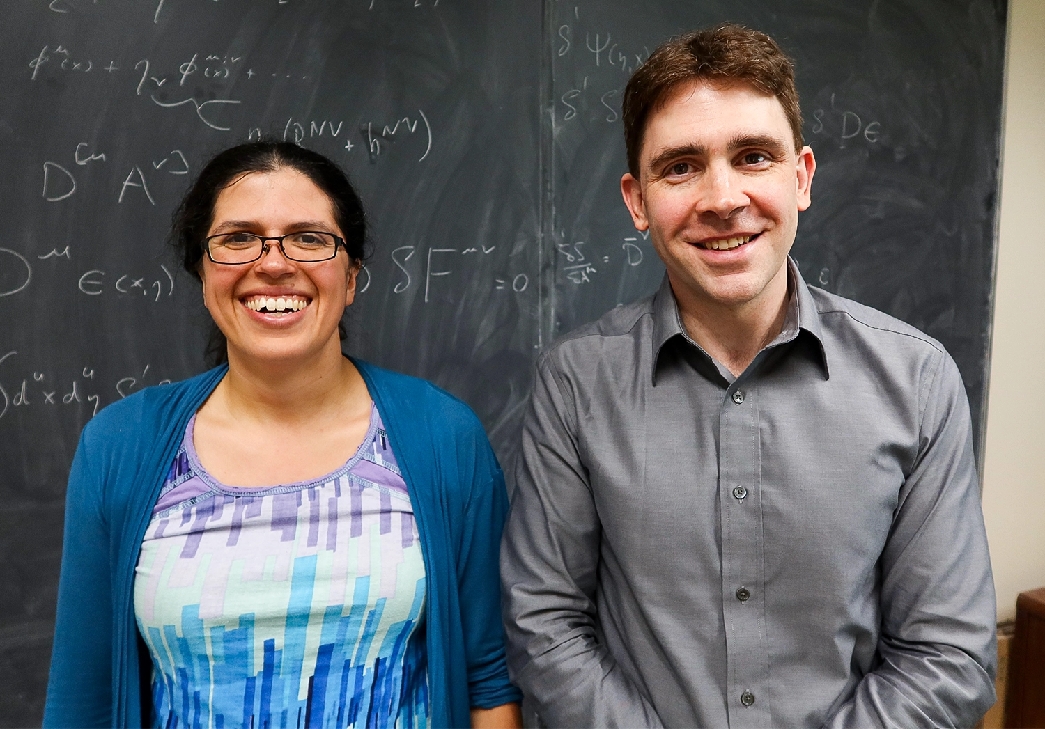 A man and woman stand side by side in front of a blackboard.